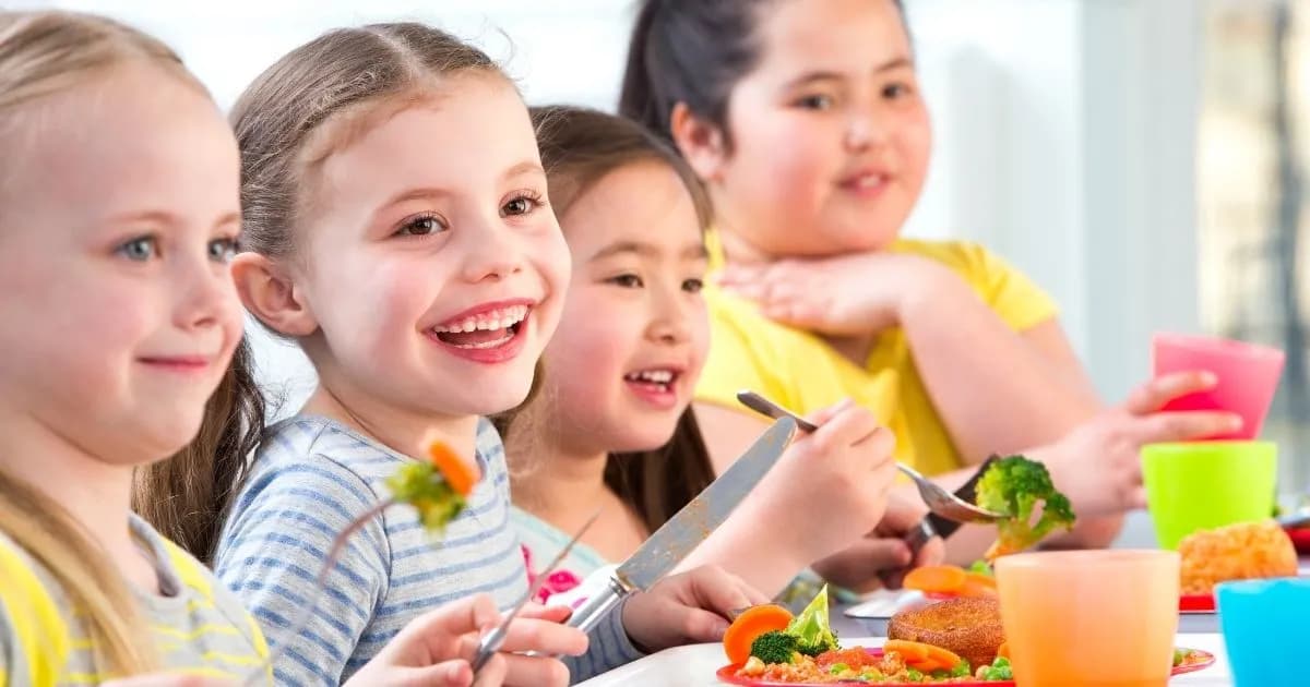 A group of cheerful young girls sitting at a table with plates of food, smiling and laughing.